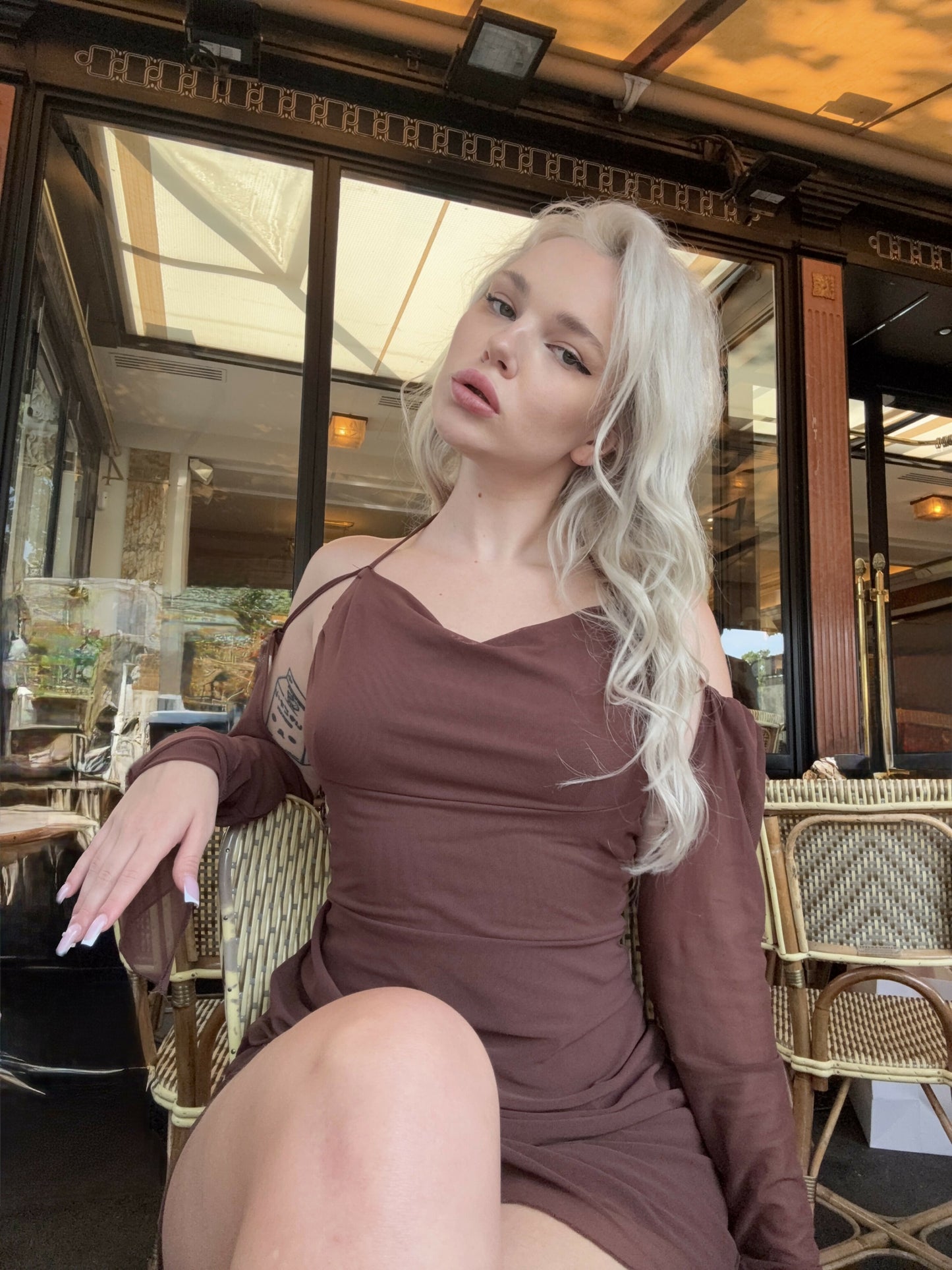 Elegant café photoshoot in Paris. Blonde model wearing a chocolate brown off-shoulder dress, sitting at a classic French bistro. Romantic, feminine and sophisticated aesthetic with soft natural lighting — ideal for fashion, lifestyle or beauty branding.
