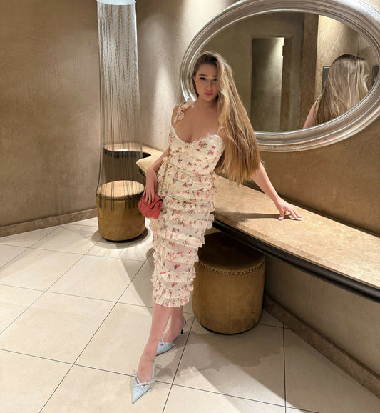 Elegant blonde woman with long flowing hair and a soft golden tan. Dressed in a delicate floral dress with ruffles, she radiates grace and confidence. Her posture is refined yet natural, embodying timeless femininity and the essence of modern elegance — p